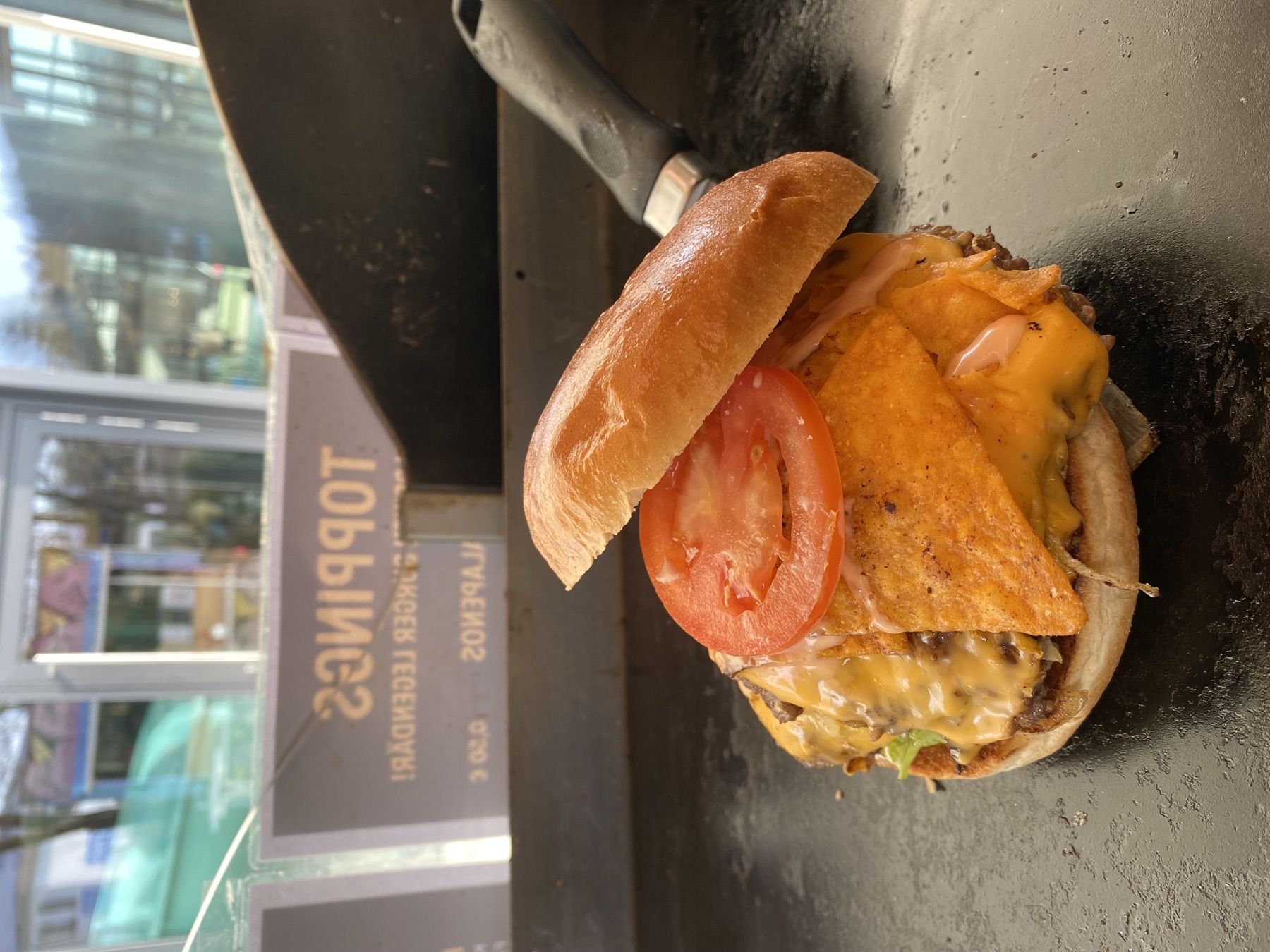 Burger mit angehobenem Bun, geschmolzenem Käse, Tomate und großen Nacho-Chips auf der Griddle