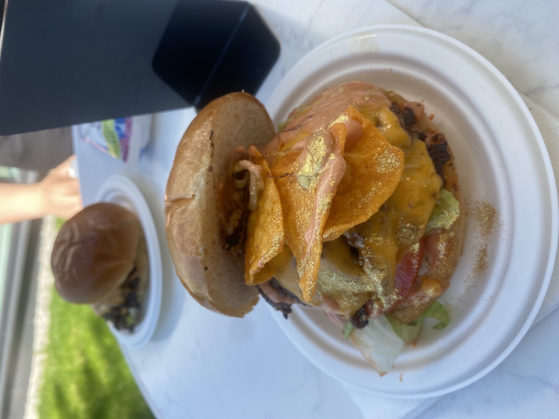 Fancy's Special mit Cheddar, Salat, Tomate, knusprigen Nacho-Chips und Goldstaub auf einem Teller im Freien