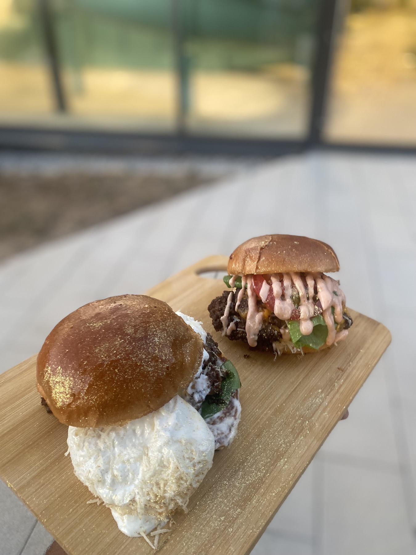 Zwei Fancy's Burger auf einem Holzbrett – einer mit Spiegelei und Käse, einer mit Salat, Tomate und Sauce